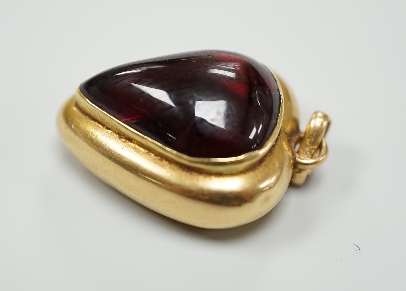 A late Victorian yellow metal (stamped 18) and cabochon garnet set heart shaped pendant, with glazed back, 22mm, gross weight 5.7 grams.